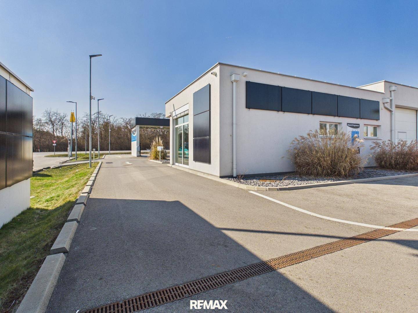 Seitenansicht des Gewerbegebäudes mit Photovoltaik-Modulen an der Fassade und Zufahrt bei sonnigem Wetter.