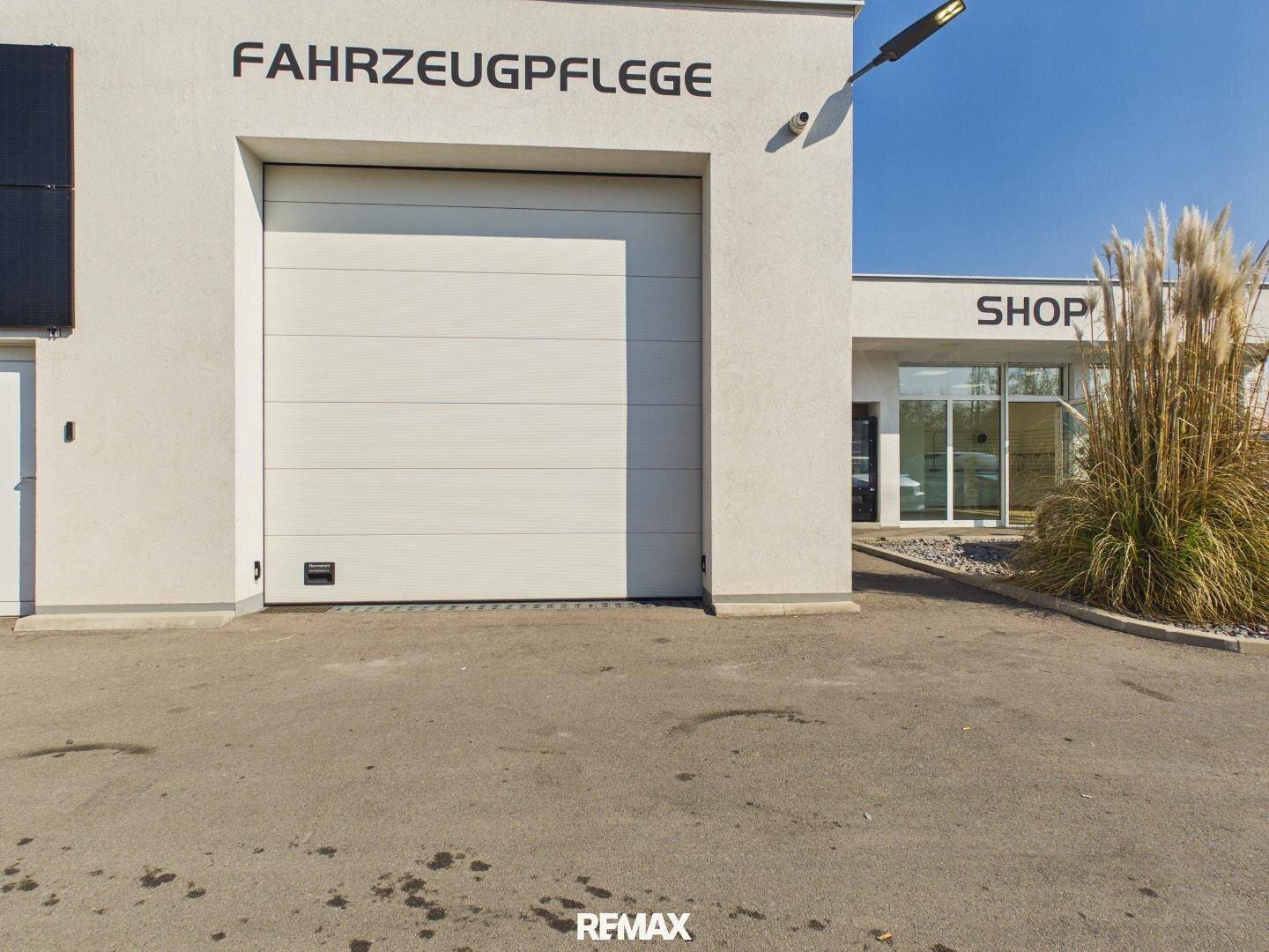 Große weiße Garagentür des Fahrzeugpflegebereichs neben dem Eingang zum Shop-Gebäude.