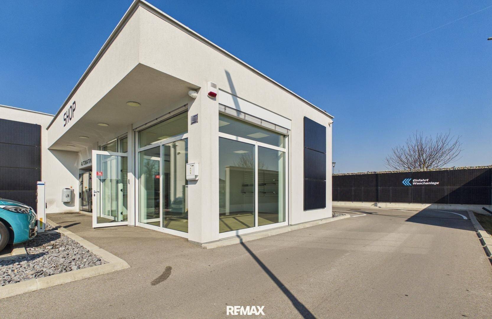 Vorderansicht des modernen Shop-Gebäudes mit großen Glasfenstern und Eingangsbereich unter blauem Himmel.