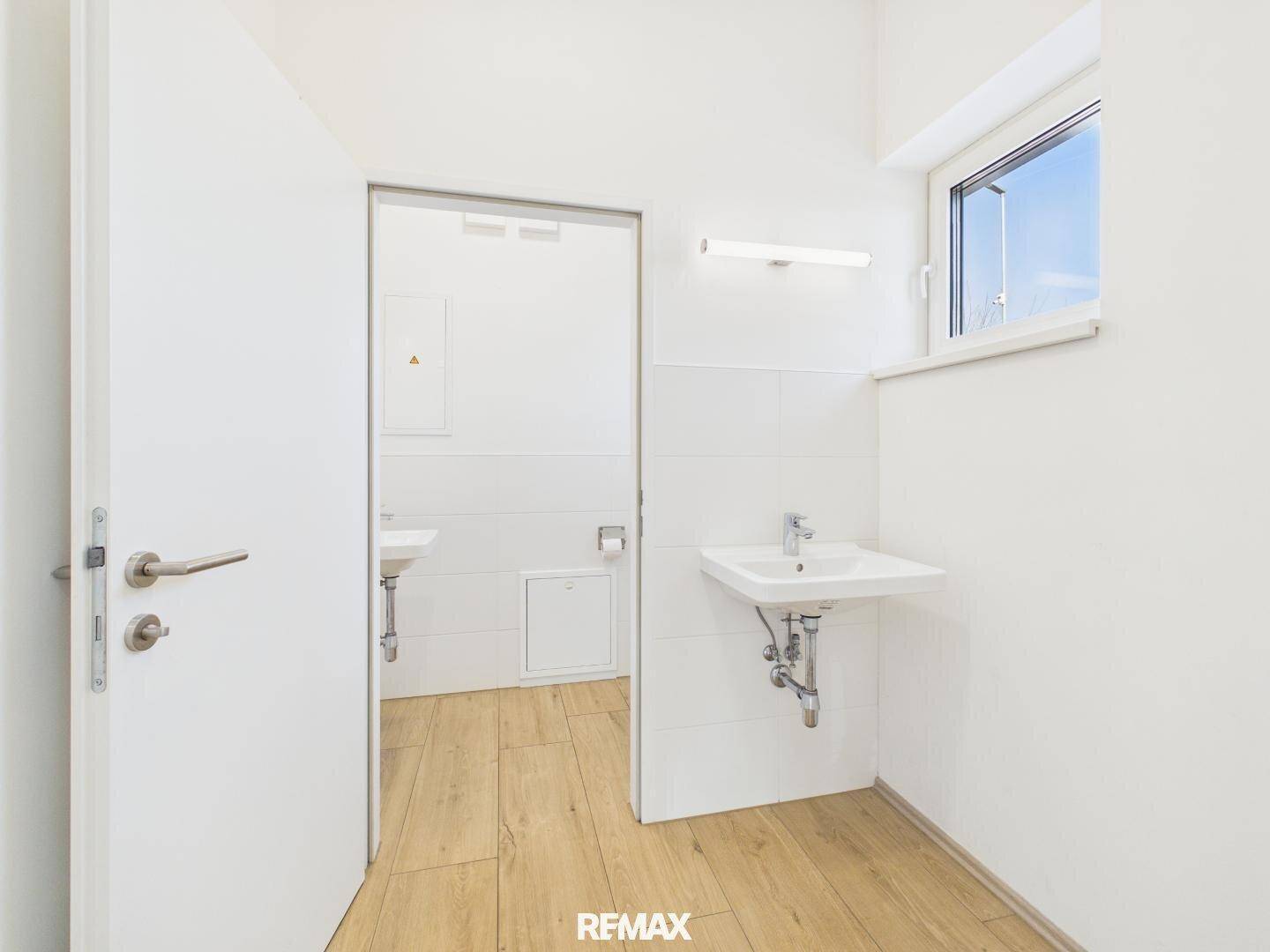 Heller Sanitärbereich mit zwei Waschbecken, Fenster und Zugang zu weiteren Räumen.