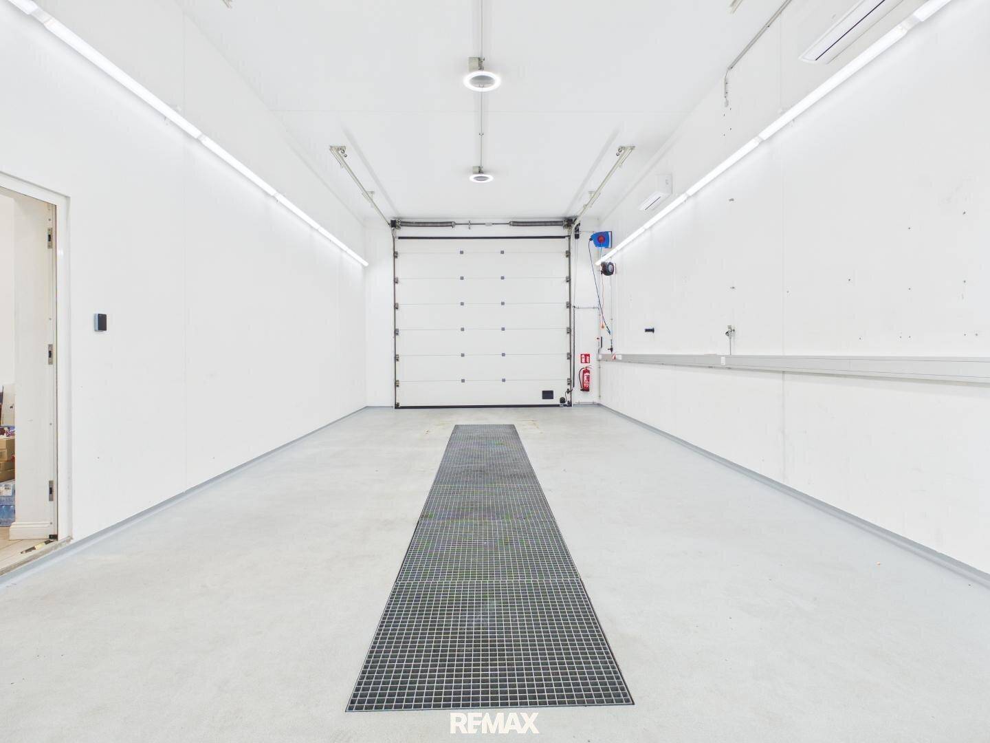Geräumige Fahrzeugaufbereitungshalle mit weiß gestrichenen Wänden, Betonboden und großem Rolltor.