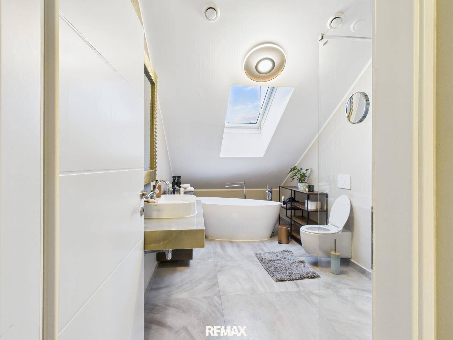 Luxuriöses Badezimmer im Dachgeschoss mit freistehender Badewanne, begehbarer Dusche und Dachfenster.