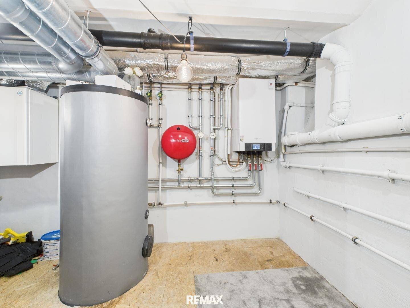Technikraum im Keller mit Heizungsanlage, Warmwasserspeicher und sichtbaren Rohren.