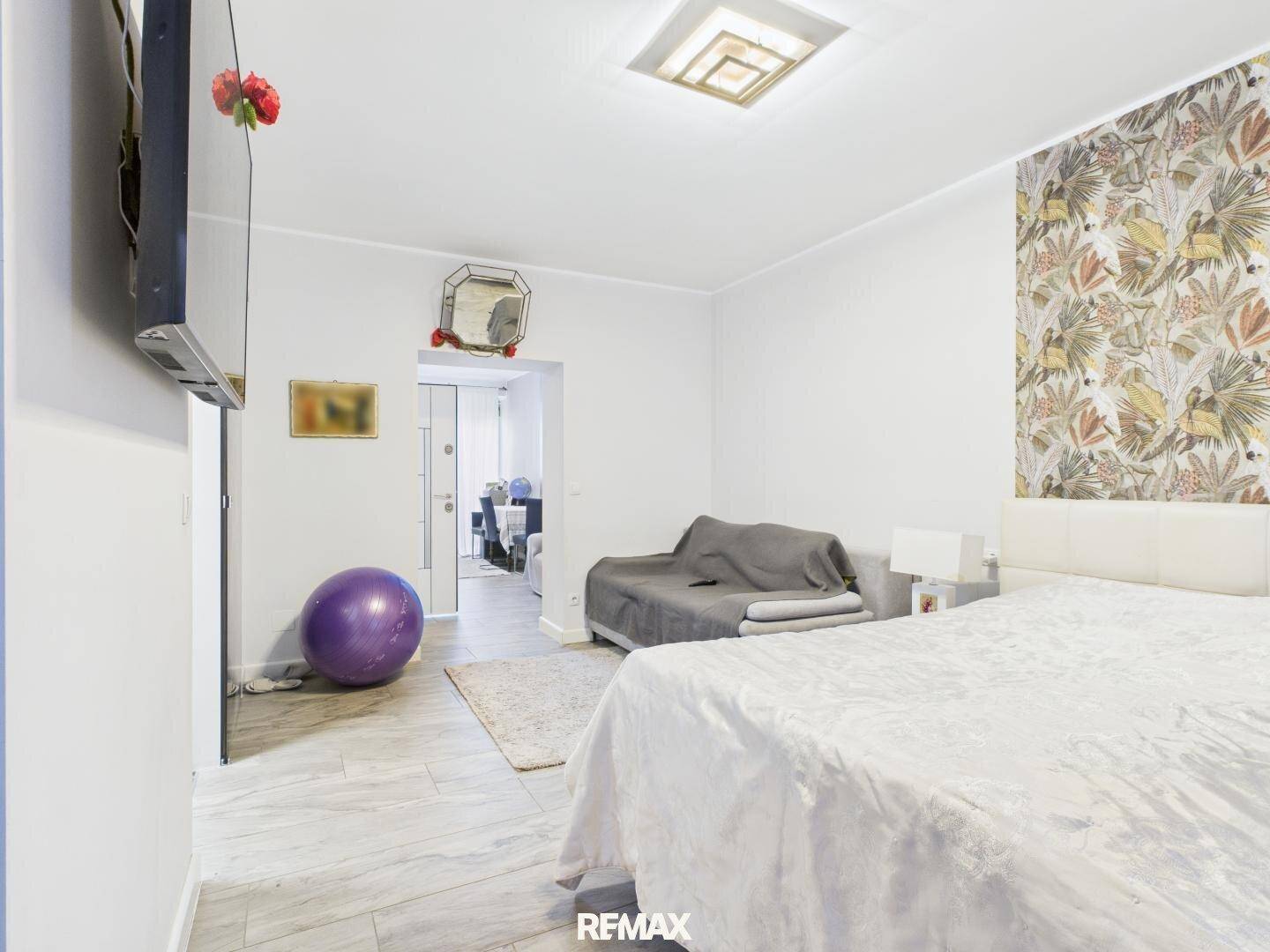 Geräumiges Schlafzimmer mit Doppelbett, kleiner Couch und großem Wandfernseher.