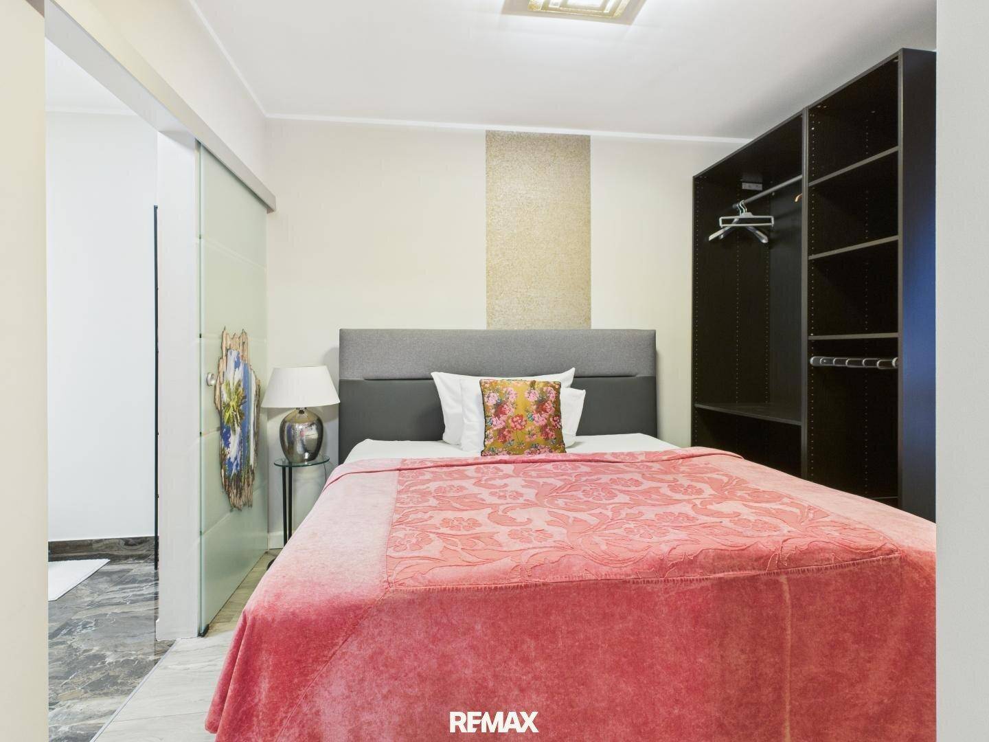 Schlafzimmer mit Doppelbett und offenem Kleiderschrank, mit Zugang zu einem weiteren Raum.
