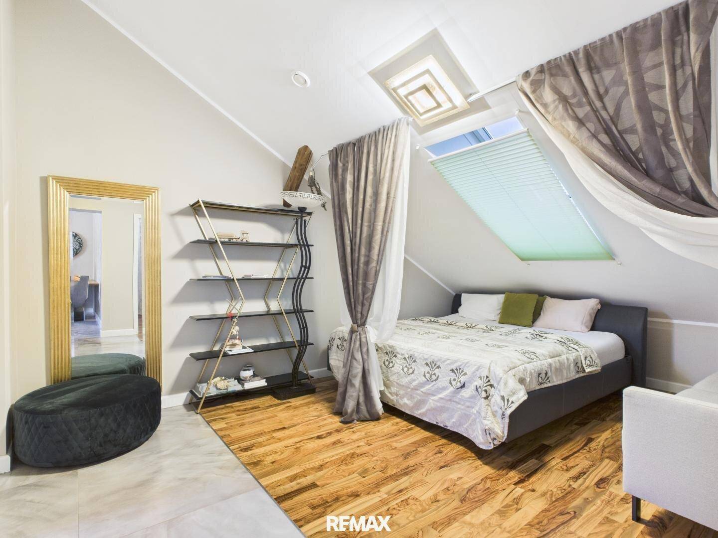 Gemütliches Schlafzimmer im Dachgeschoss mit Dachfenster, Holzboden und großem Spiegel.