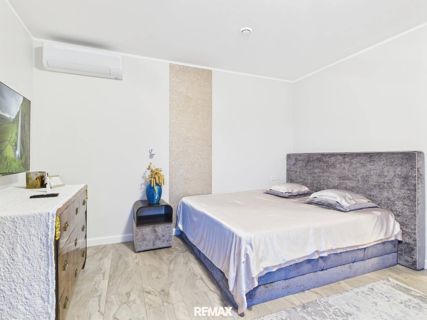 Modernes Schlafzimmer mit großem Bett, Kommode und Wandfernseher.