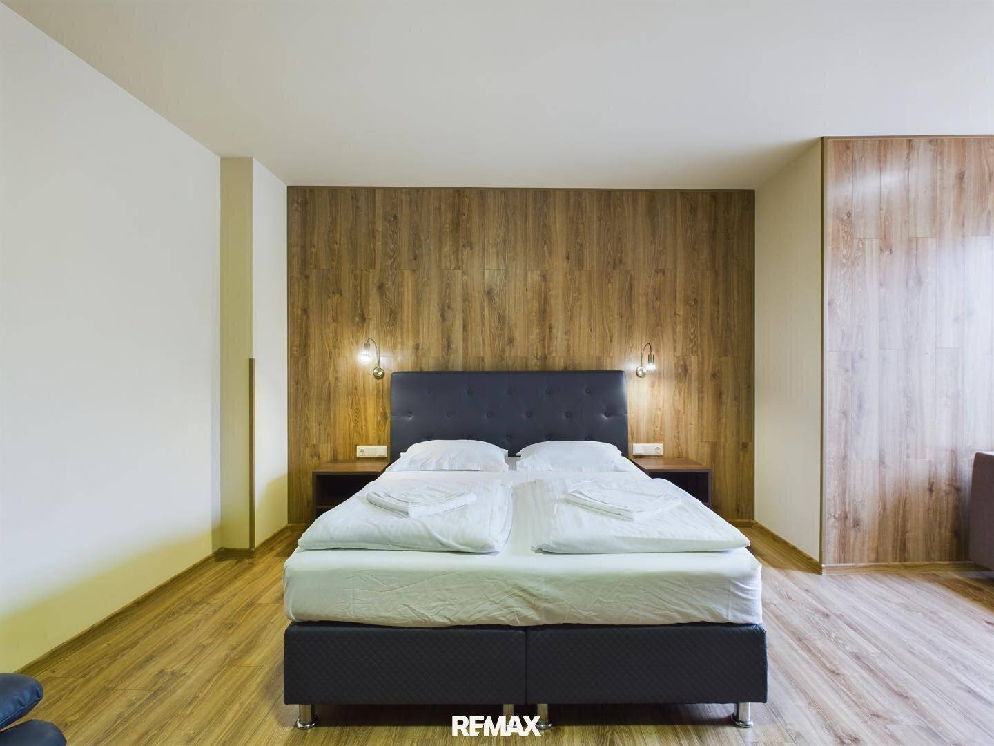 Modernes Schlafzimmer mit Holzwand hinter dem Bett, Holzboden und zwei Nachttischen mit Lampen.