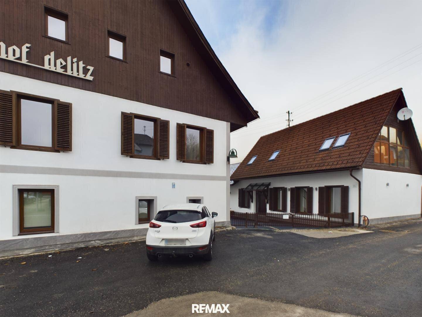 Blick auf den Gasthof Delitz und das angrenzende Gebäude mit Dachfenstern und Parkplätzen.