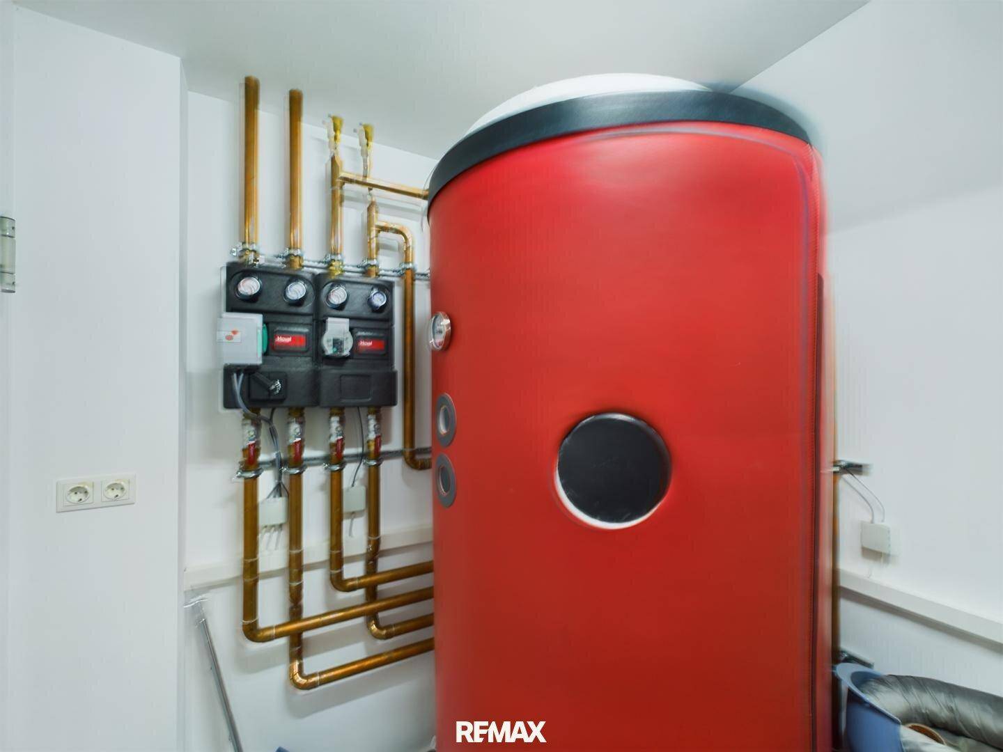 Heizungsraum mit einem großen roten Warmwasserspeicher und sichtbaren Kupferrohren.