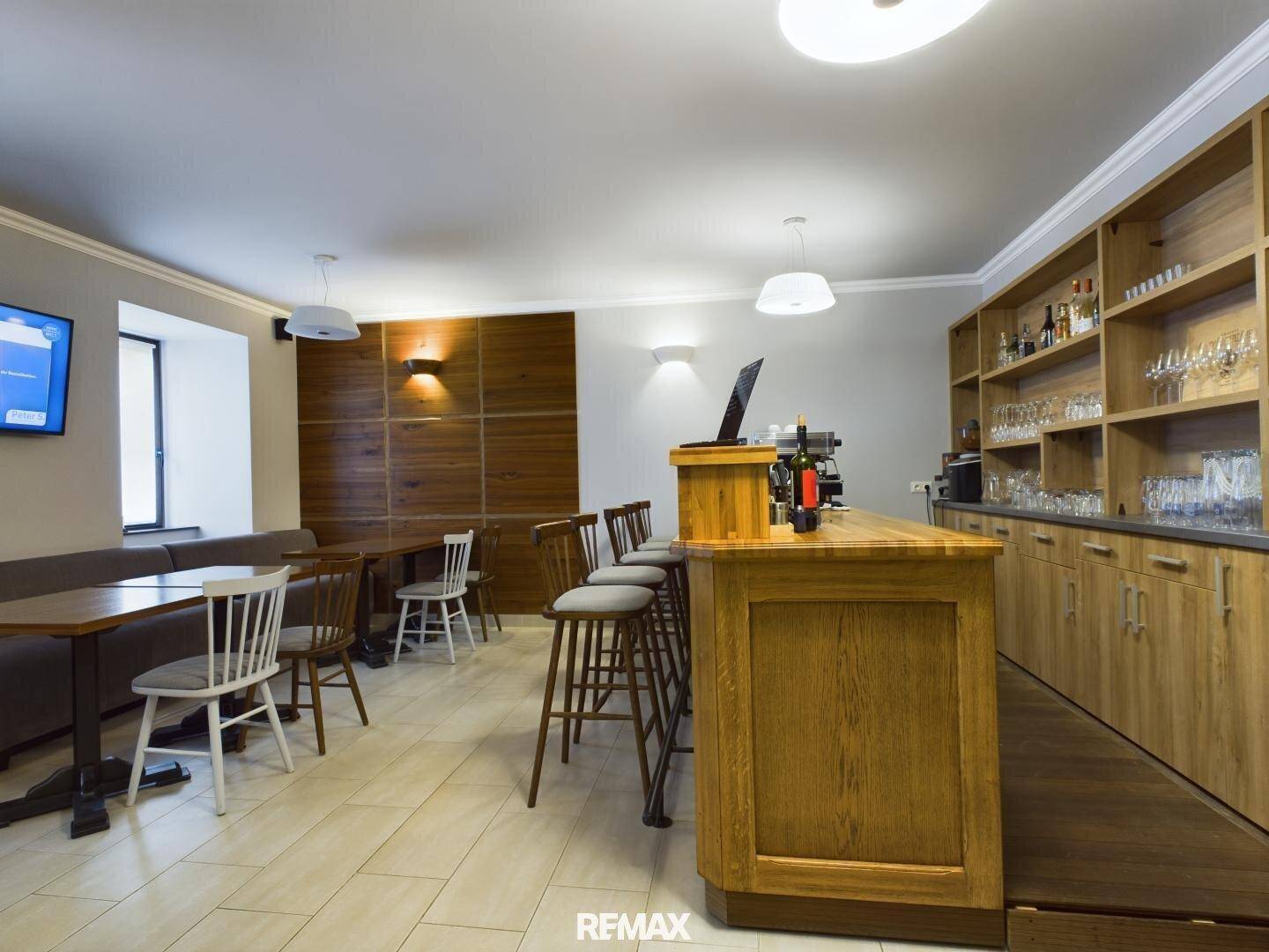 Bar- und Essbereich mit Holztresen, Regalen für Gläser und Flaschen sowie Sitzgelegenheiten.