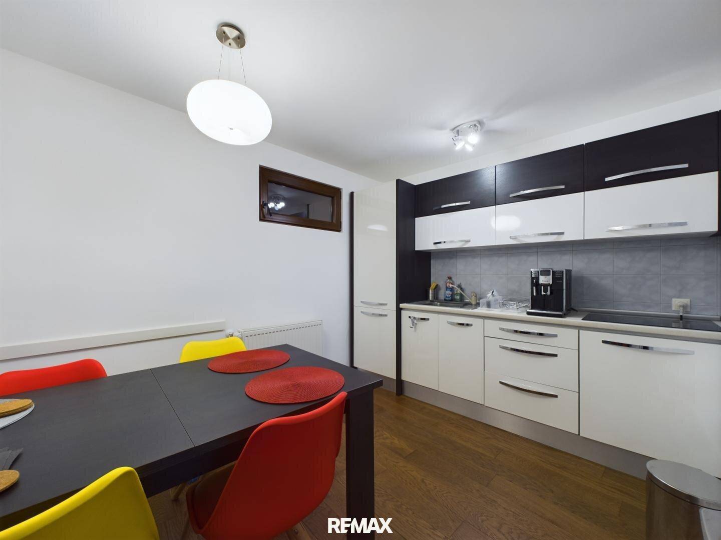 Moderne Küche mit schwarz-weißen Schränken, Holzboden und einem Esstisch mit bunten Stühlen.