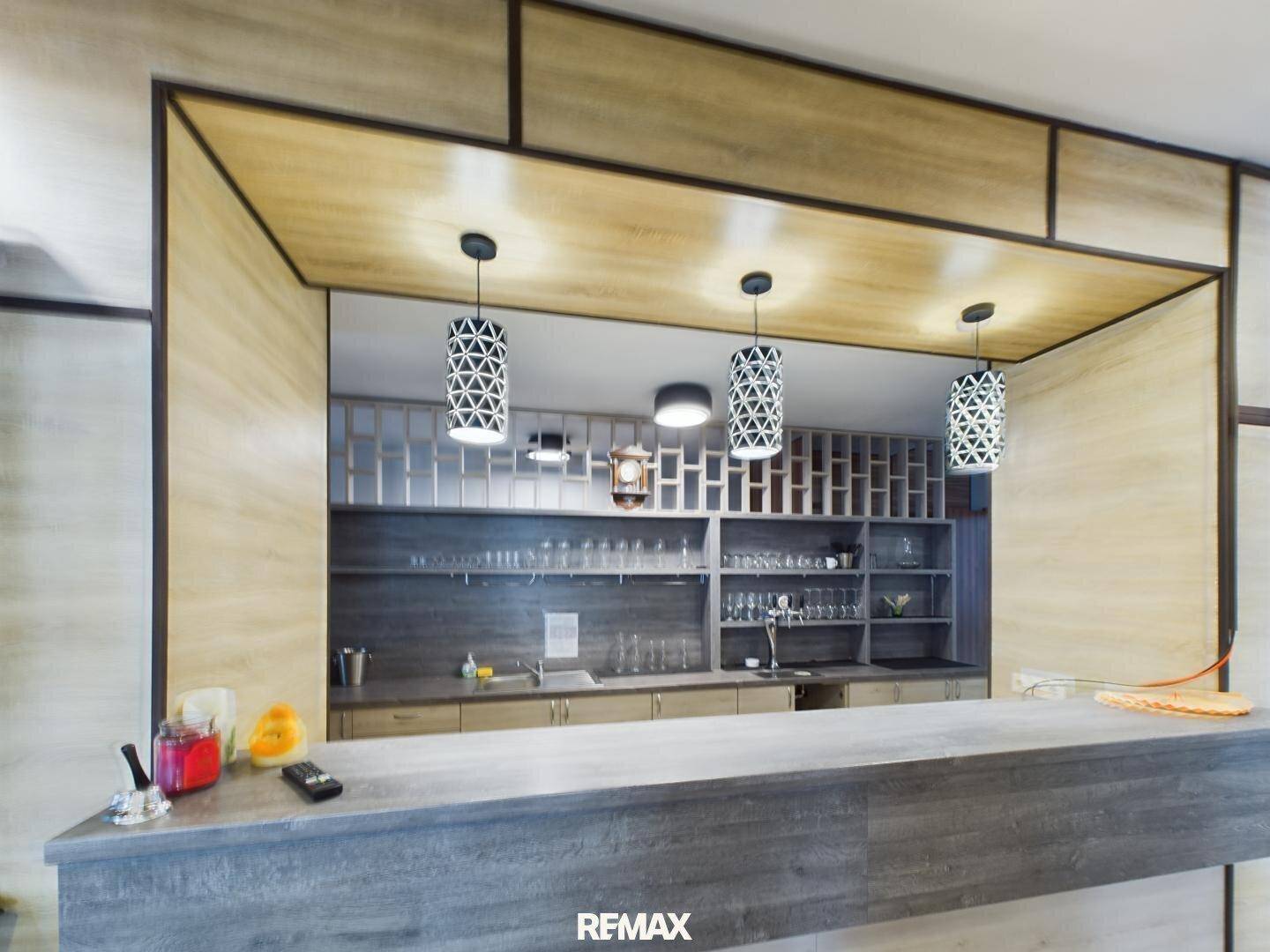 Moderne Bar mit Holztheke, Regalen für Gläser und Flaschen sowie stilvollen Hängelampen.
