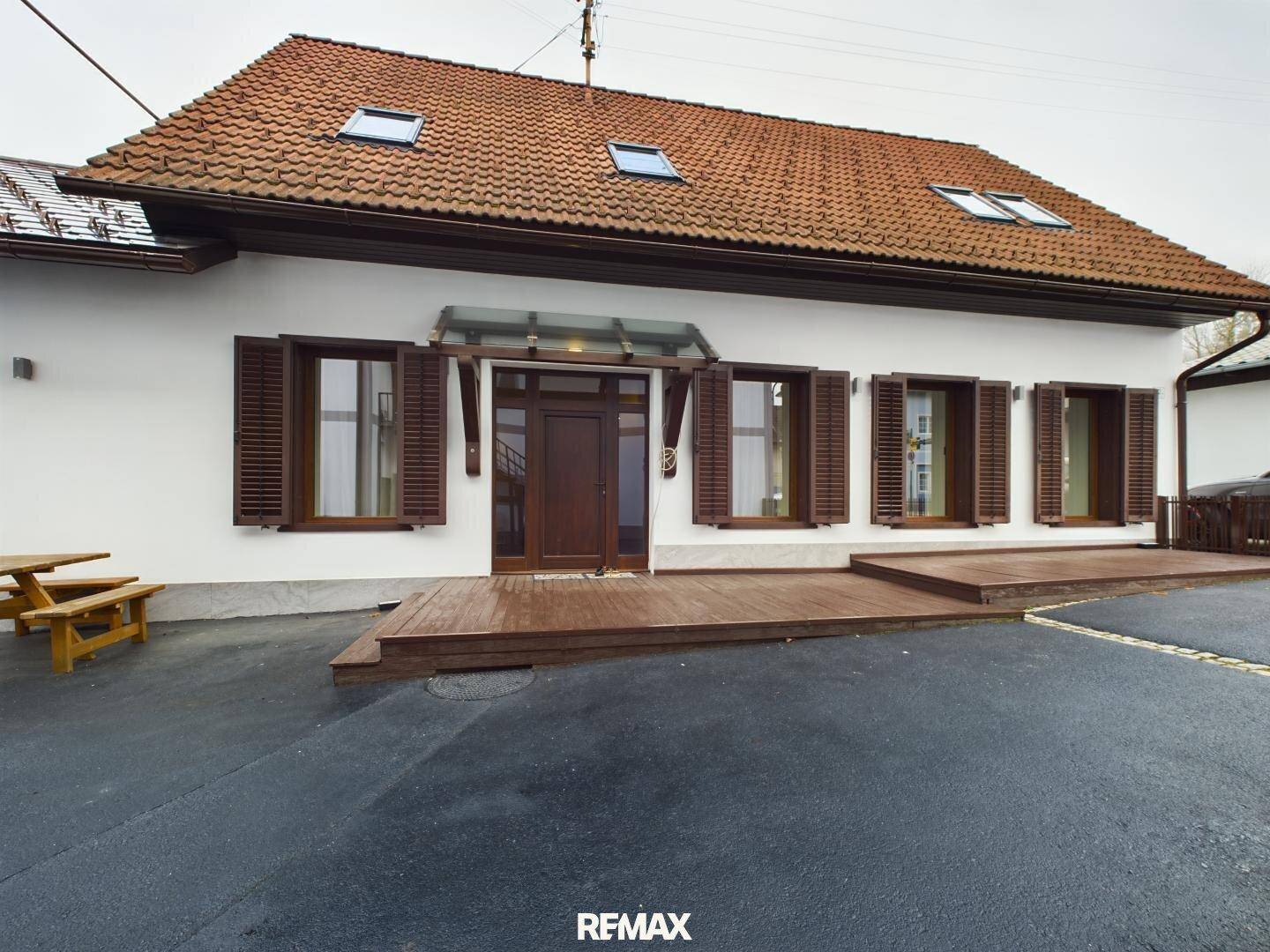 Traditionelles Haus mit rotem Ziegeldach, Holzfensterläden und einer Holzterrasse.