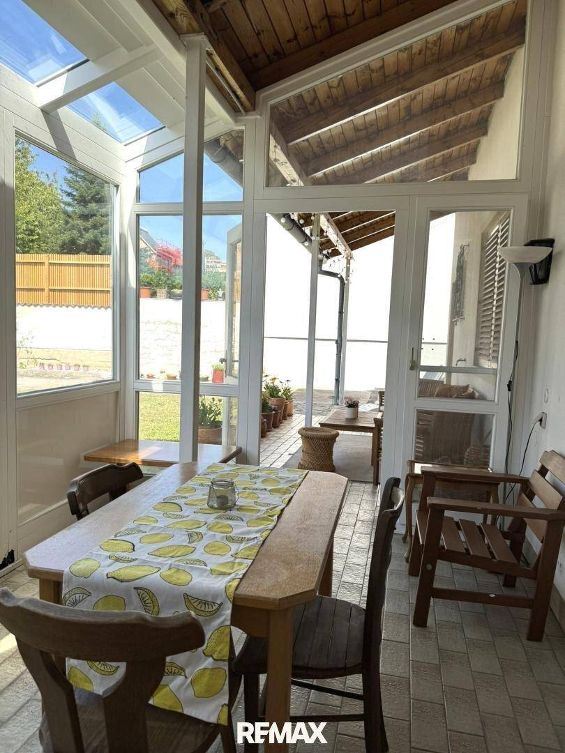 Heller Wintergarten mit Esstisch, Holzdecke und Blick in den Garten.