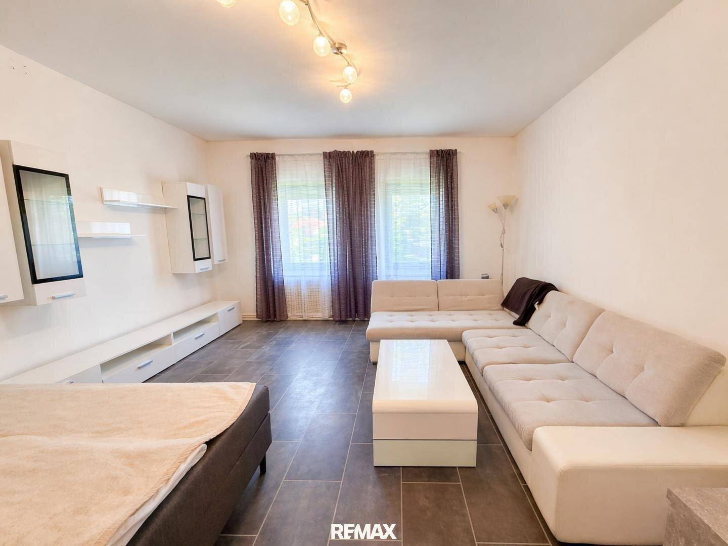 Modern eingerichtetes Wohnzimmer mit großem Sofa und dunklem Fliesenboden.