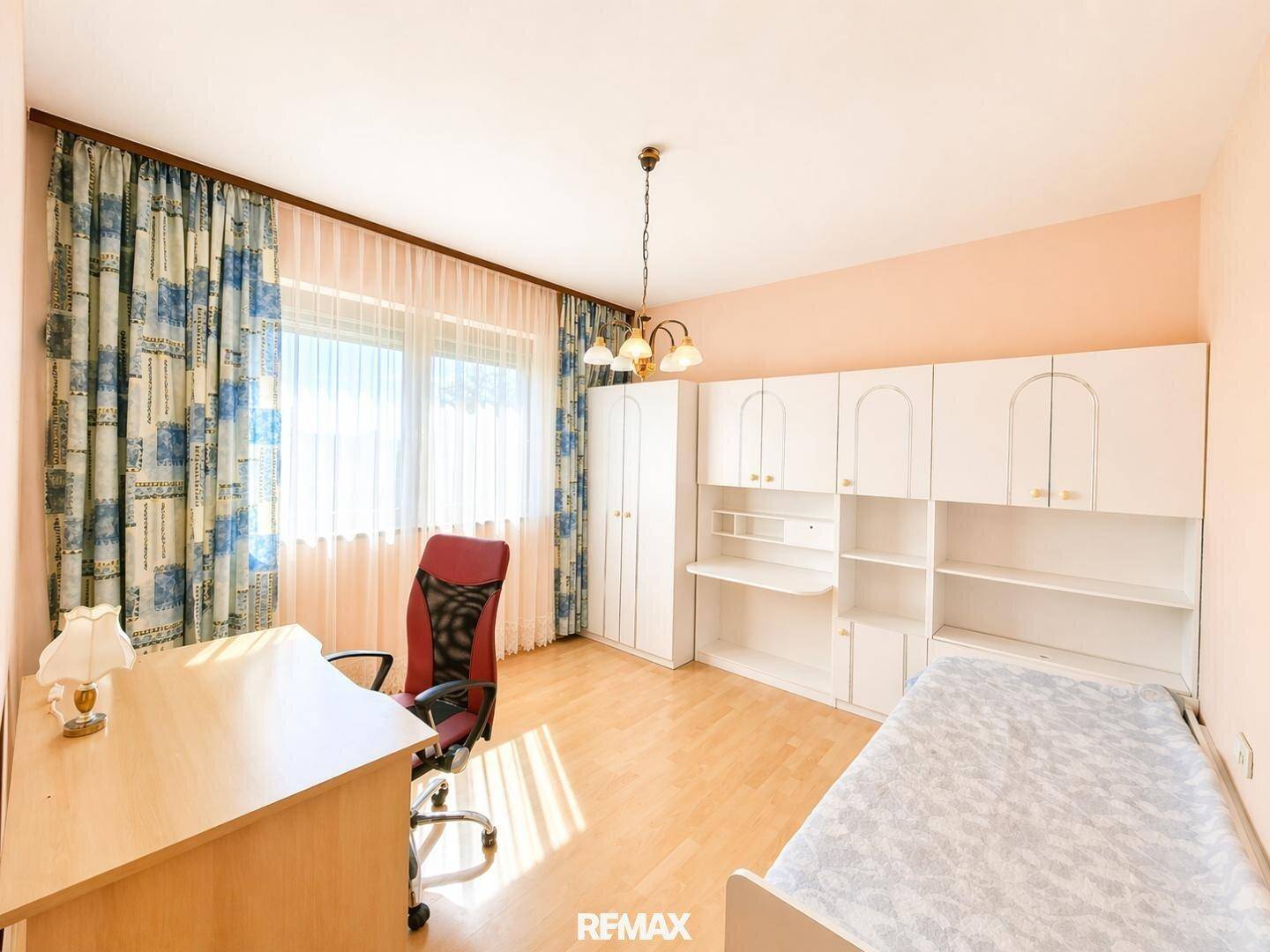 Helles Arbeitszimmer mit Laminatboden, Schreibtisch und einem weißen Regalsystem.