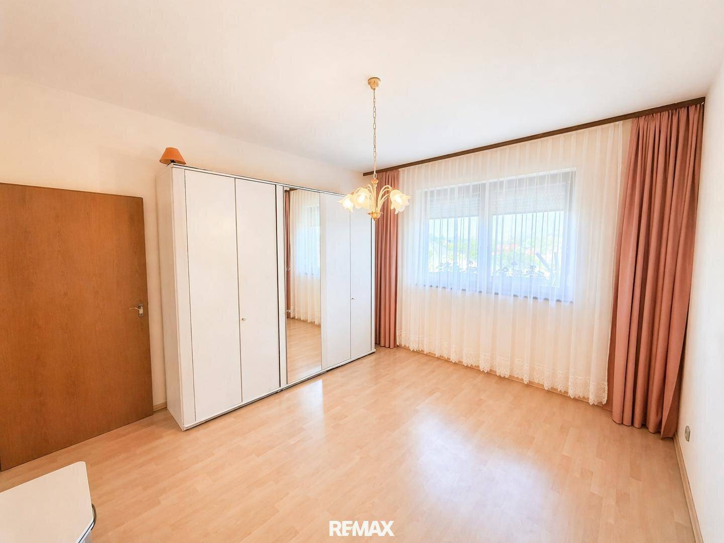 Helles Schlafzimmer mit Laminatboden, weißem Kleiderschrank und großem Fenster.