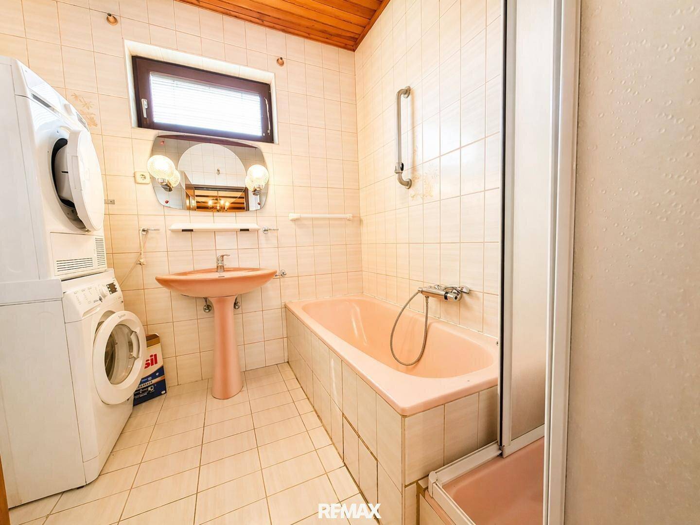 Funktionales Badezimmer mit rosa Badewanne, Dusche, Waschmaschine und Trockner.