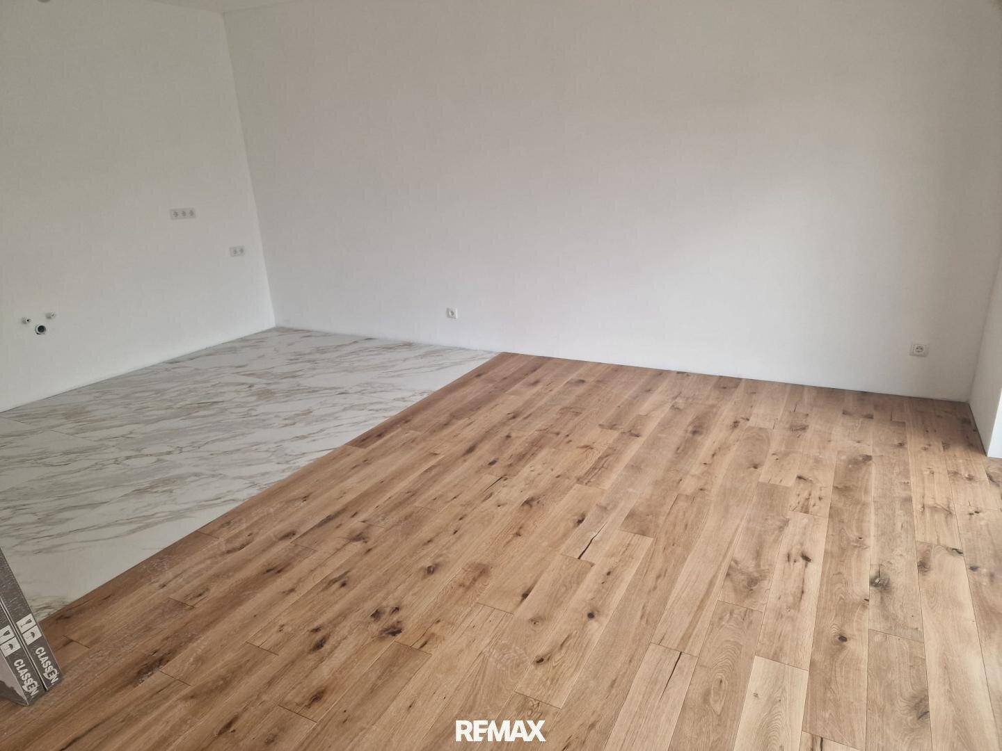 Heller Raum mit teilweise verlegtem Holz- und Fliesenboden, der auf die Fertigstellung wartet.