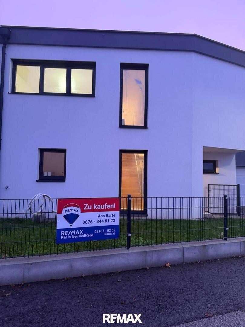 Modernes Haus bei Dämmerung mit einem "Zu kaufen!" Schild vor der Fassade.