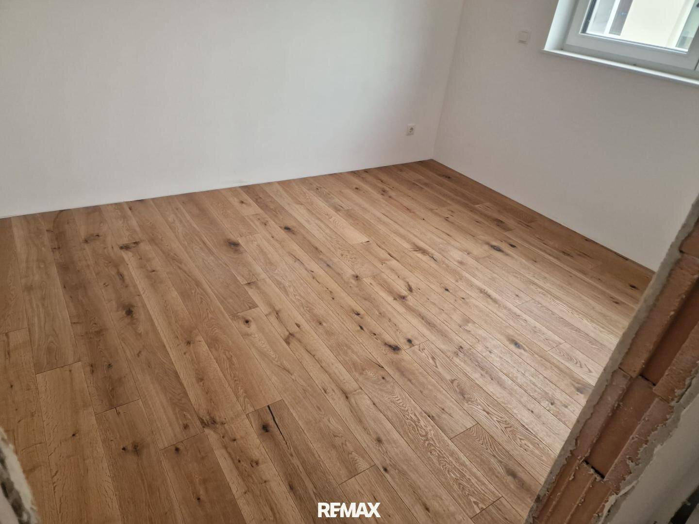 Leerer Raum mit hellem Holzfußboden und weißen Wänden, bereit für die individuelle Gestaltung.