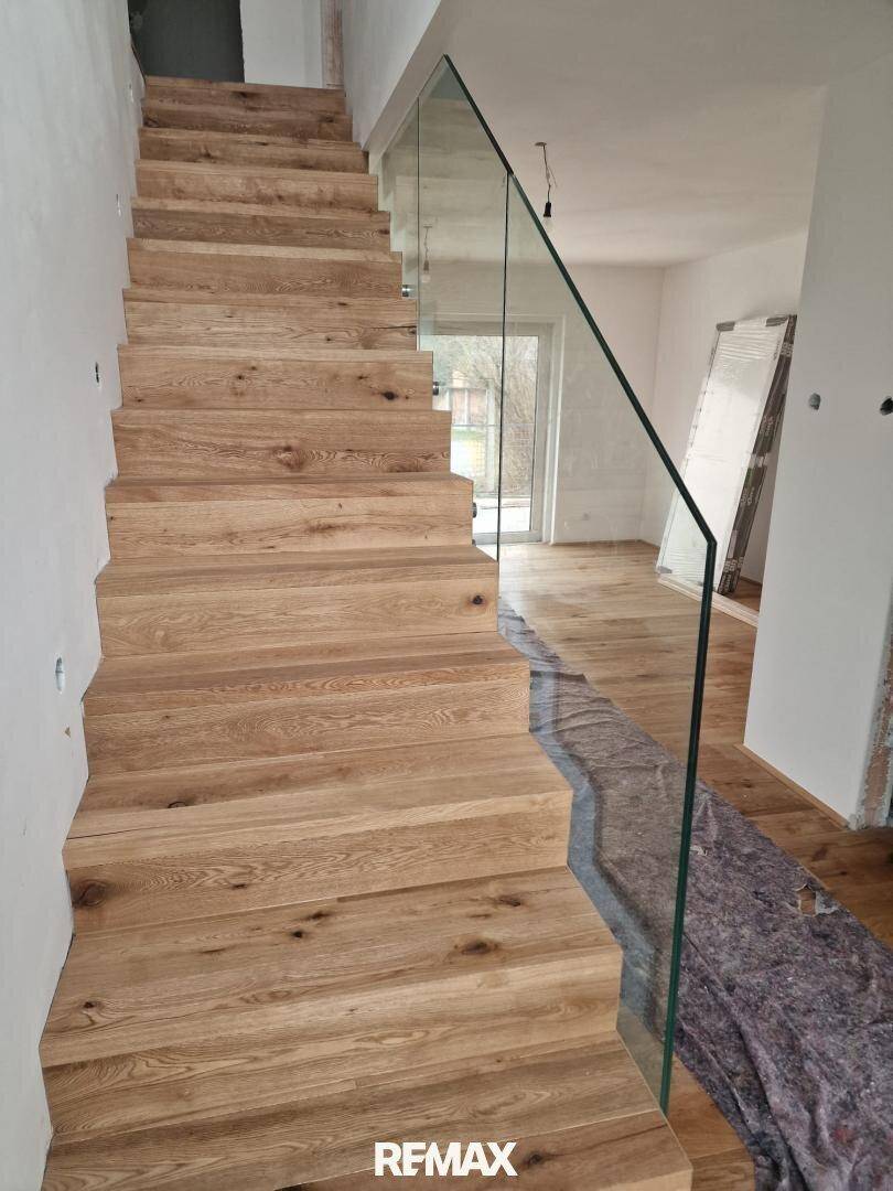 Elegante Holztreppe mit moderner Glasbrüstung in einem hellen Eingangsbereich des Hauses.