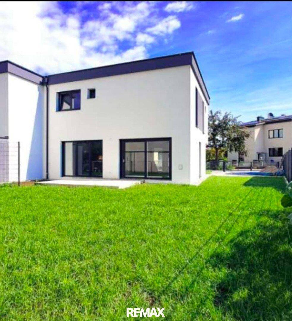 Hinteransicht des modernen Hauses mit großem Rasenbereich und bodentiefen Fenstern zum Garten.