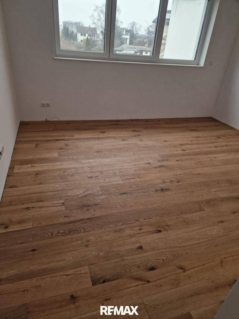 Geräumiger Raum mit hellem Holzfußboden und einem Fenster, das viel Tageslicht hereinlässt.