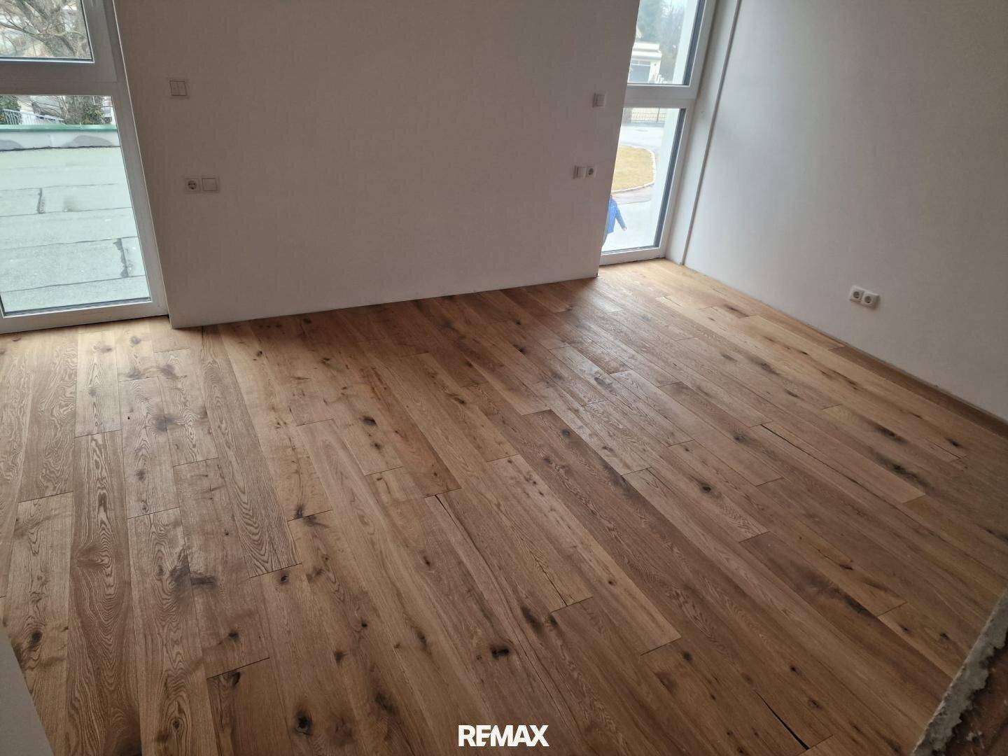 Heller Raum mit Holzboden und großen Fenstern, die Zugang zum Außenbereich bieten.