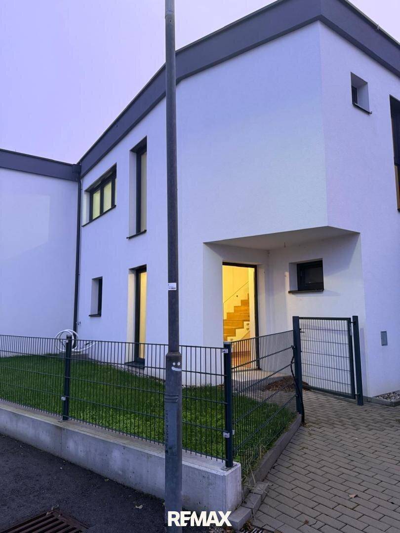 Eingangsbereich eines modernen Hauses bei Dämmerung, mit beleuchteter Treppe im Inneren.