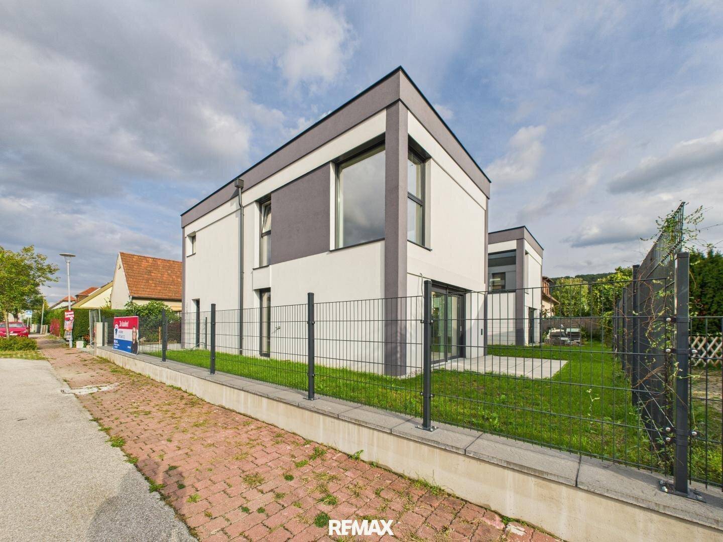 Neubau mit moderner Fassade, umzäuntem Gartenbereich und Gehweg.