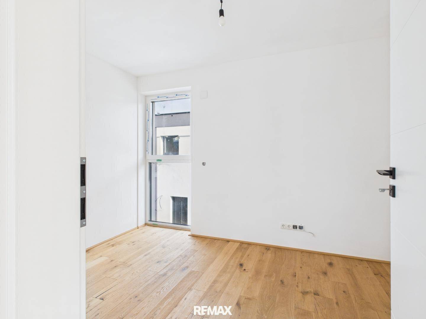 Helles Zimmer mit Holzboden und einem Fenster, das Tageslicht spendet.