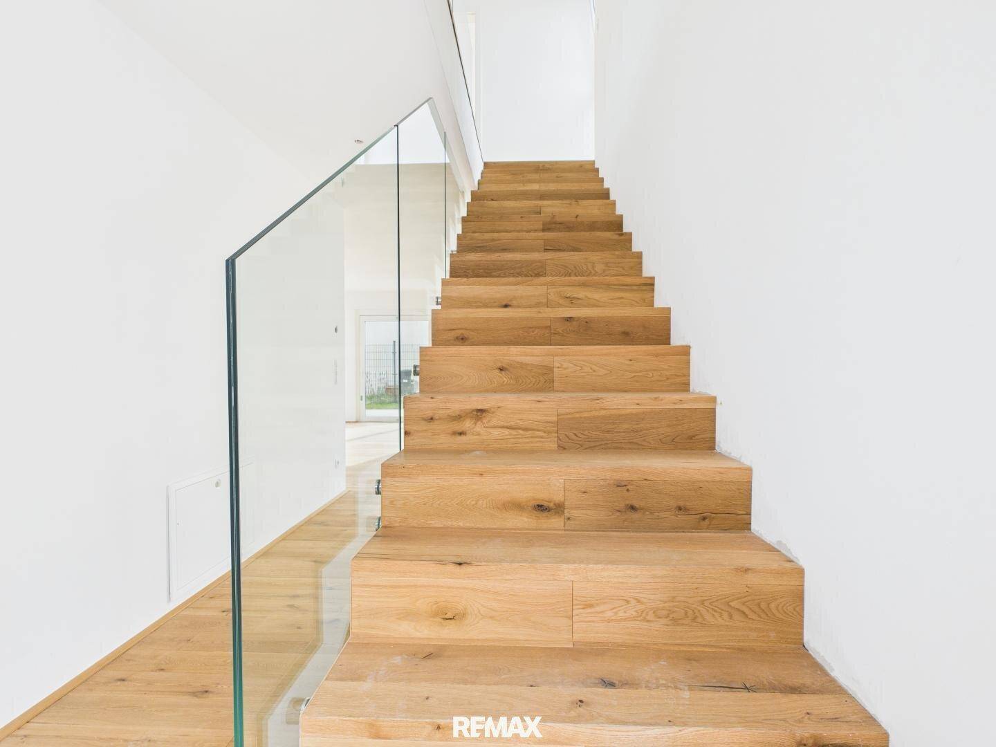 Moderne Holztreppe mit Glasgeländer in einem hellen Innenraum.