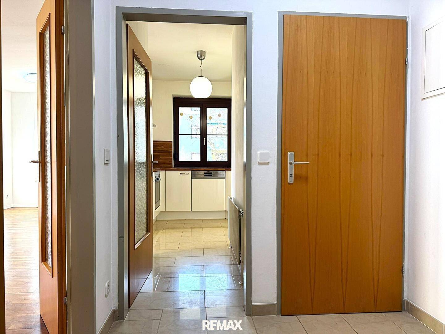 Heller Flur mit Blick in eine moderne Küche mit weißen Schränken und Holztheke.