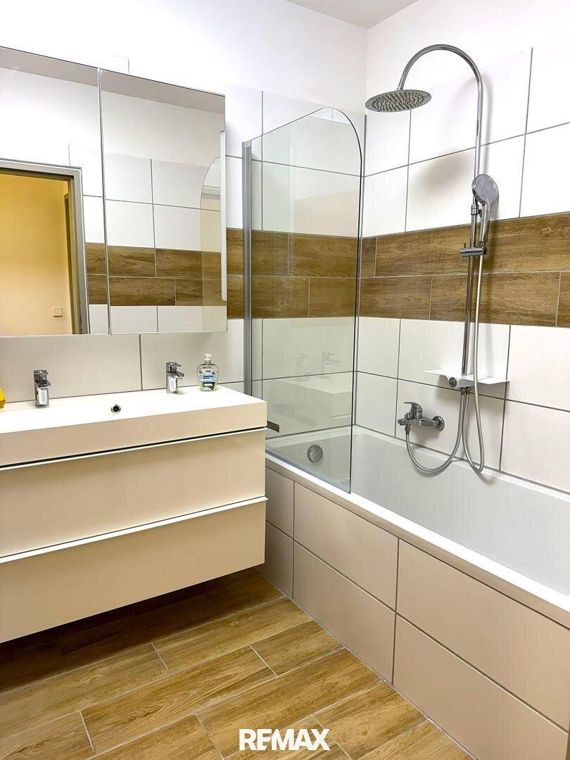 Modernes Badezimmer mit Badewanne, Duschvorrichtung, Einzelwaschbecken und Spiegelschrank.