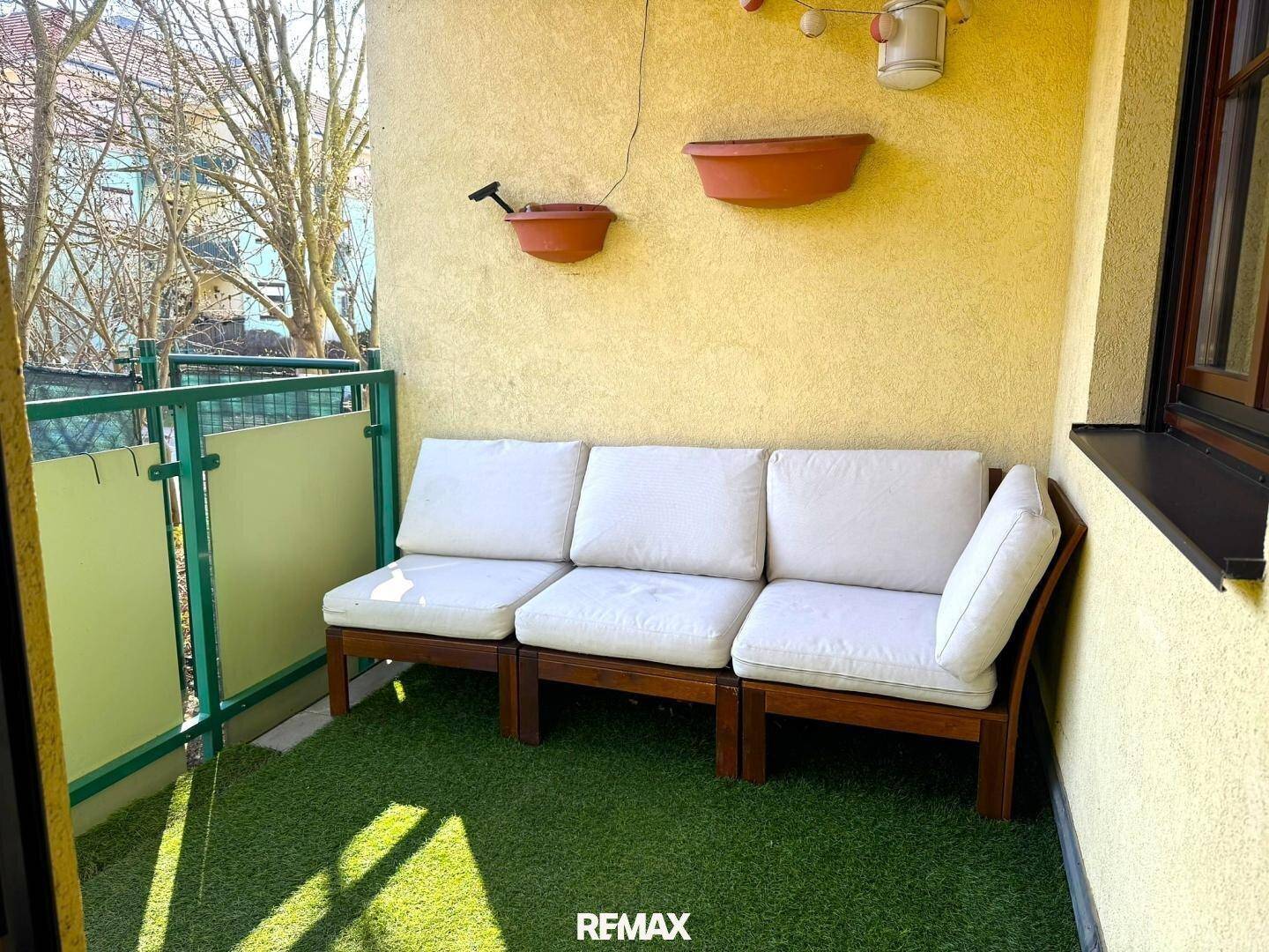 Gemütlicher Balkon mit Kunstrasen, bequemer Sitzgelegenheit und gelber Fassade.