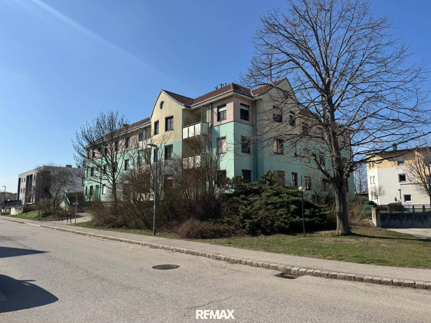 Mehrfamilienhaus mit farbiger Fassade, umgeben von Bäumen und Sträuchern an einem sonnigen Tag.