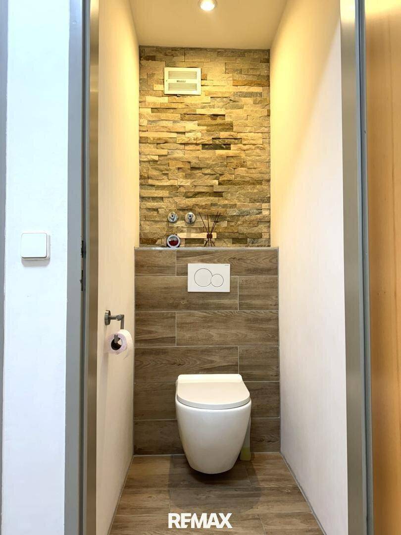 Modernes Gäste-WC mit wandhängender Toilette, stilvollen Fliesen und Steinakzenten.