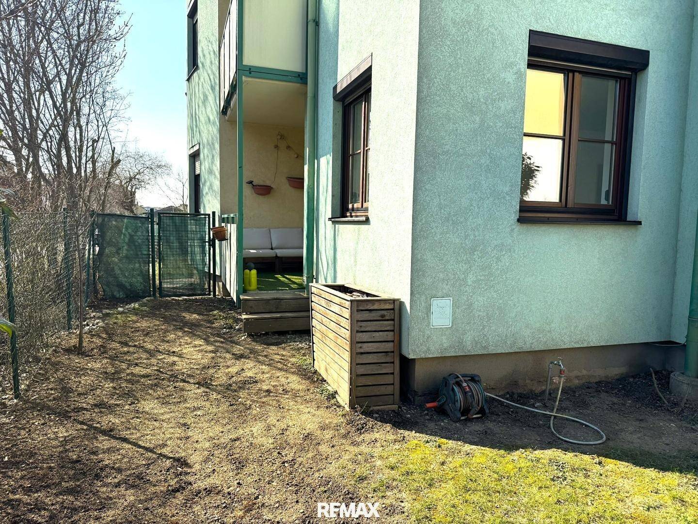 Kleiner Gartenbereich neben dem Gebäude mit Rasenfläche und einem Holzkasten.