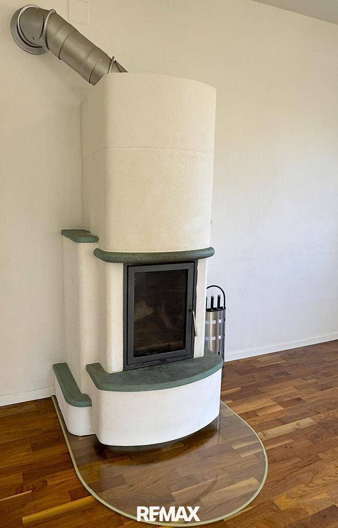 Detailansicht eines traditionellen Kachelofens mit moderner Glastür und schützender Glasplatte.