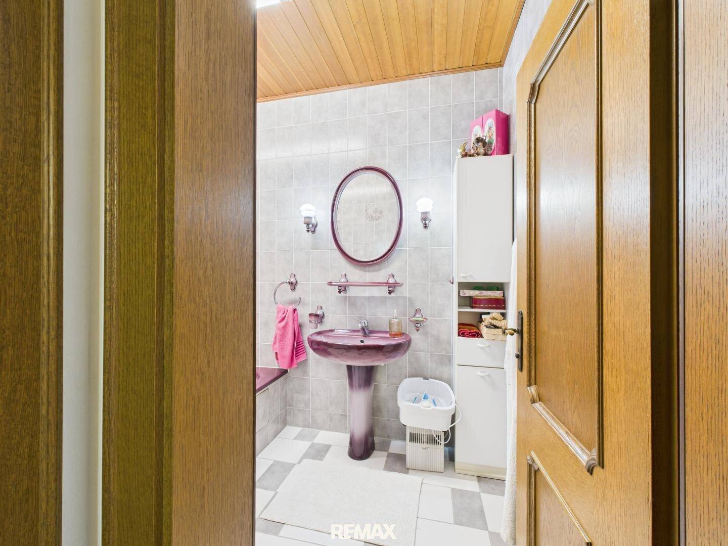 Kleines Badezimmer mit rosa Standwaschbecken, ovalem Spiegel und Holzdecke.