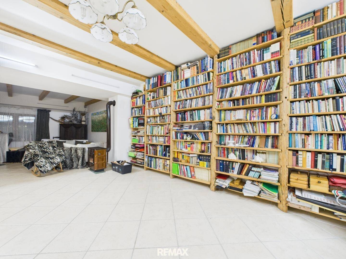 Geräumige Bibliothek mit raumhohen Bücherregalen, Holzbalkendecke und Kaminofen.