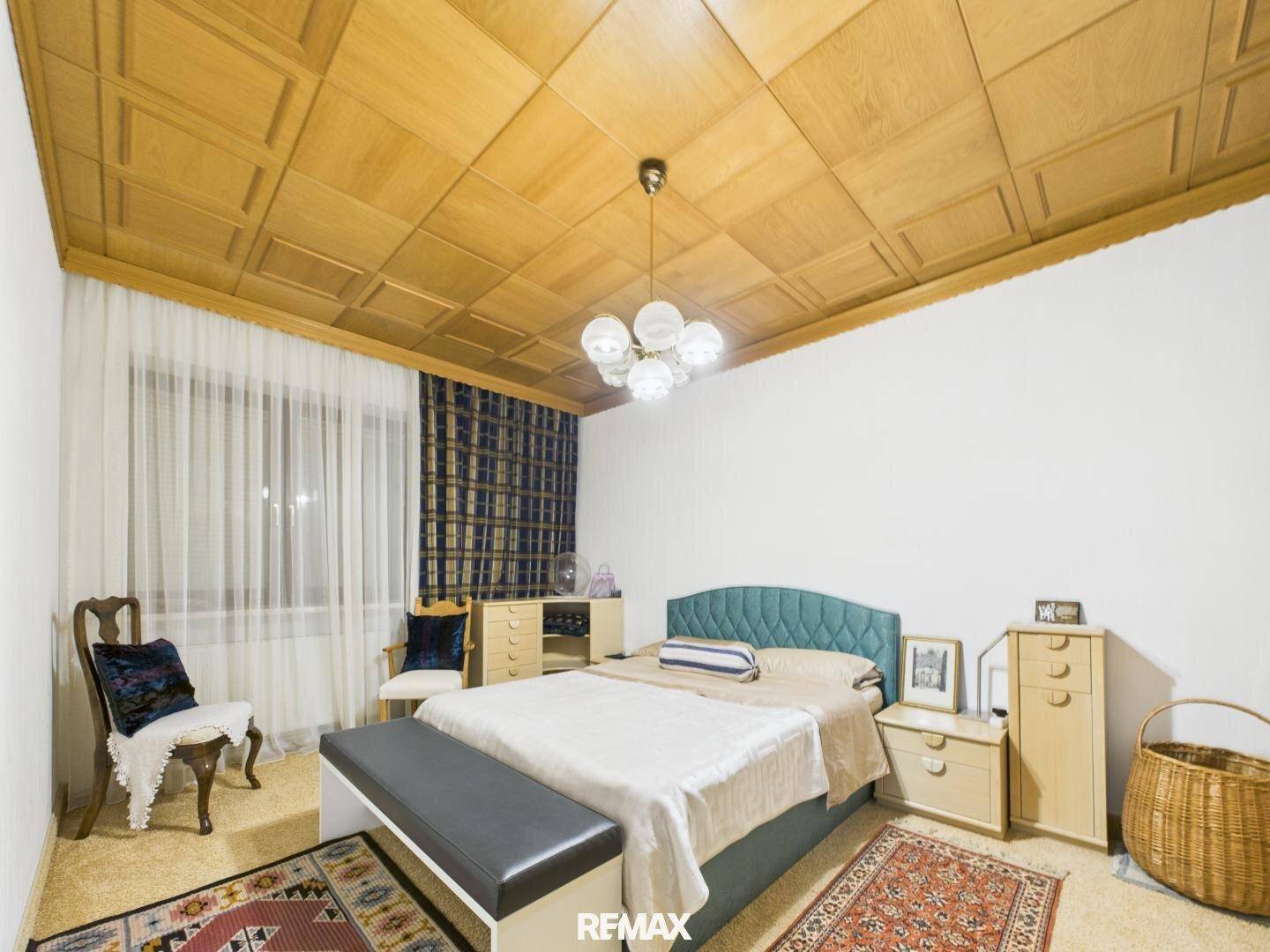 Helles Schlafzimmer mit Holzkassettendecke, Parkettboden und modernem Bett.