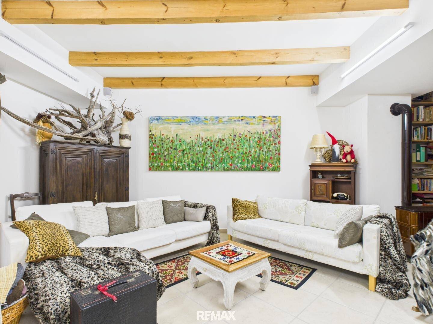 Geräumiges Wohnzimmer mit Holzbalken an der Decke, hellen Sofas und dekorativen Elementen.