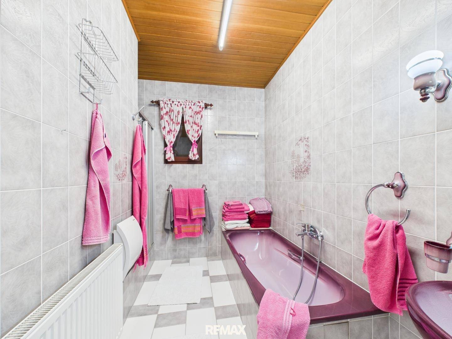 Badezimmer mit rosa Badewanne, passendem Waschbecken und hellgrauen Fliesen.