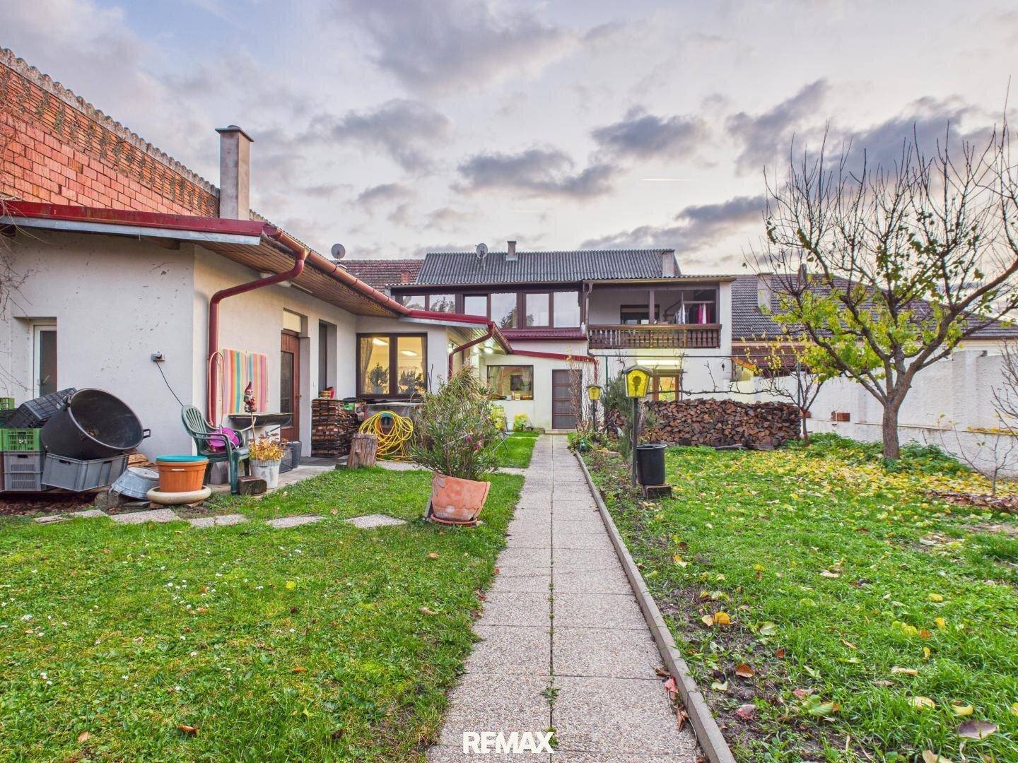 Großer Gartenbereich mit Rasenfläche, Holzstapel und Blick auf die Rückseite des Hauses.