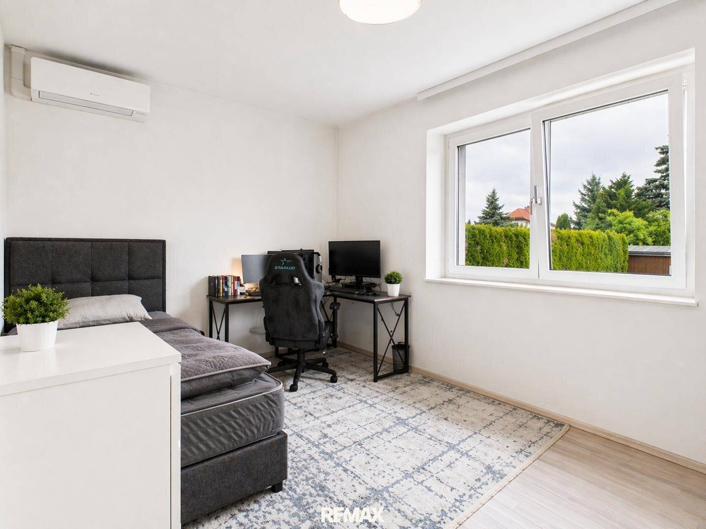 Helles Schlafzimmer mit Einzelbett, Schreibtisch und Blick ins Grüne durch das Fenster.
