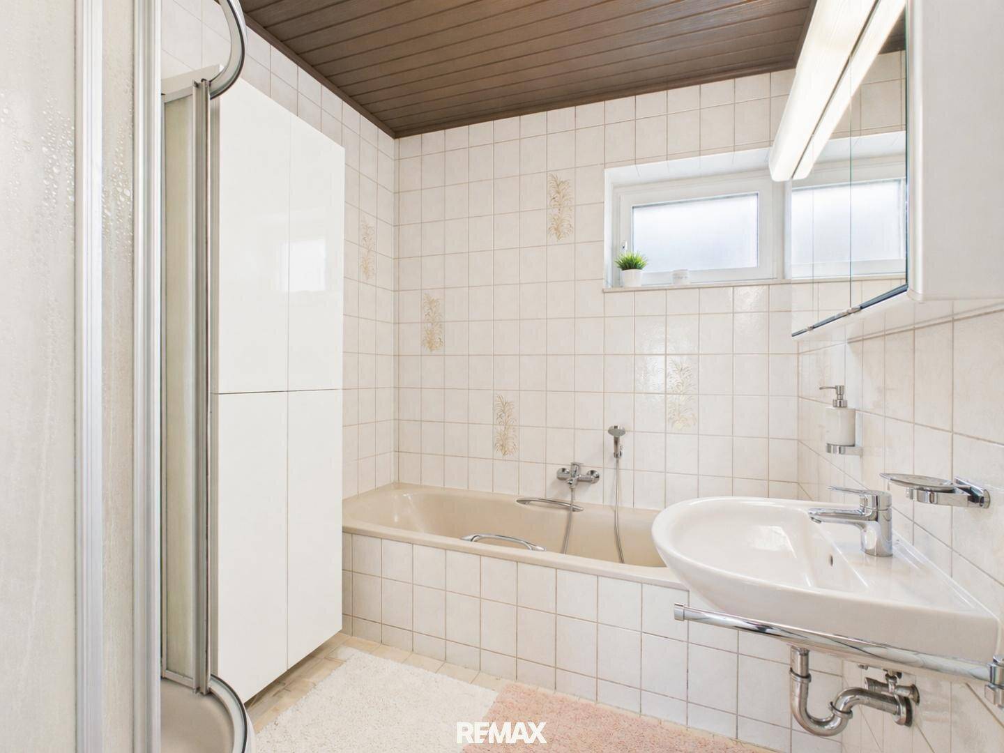 Badezimmer mit Badewanne, Dusche, Waschbecken und Fenster, gefliest in hellem Design.
