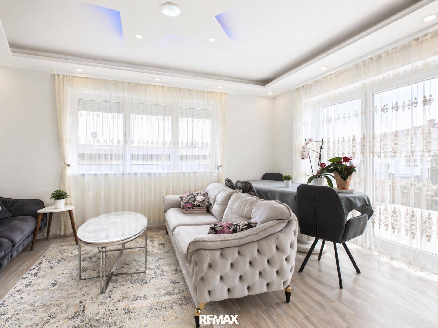 Helles Wohn- und Esszimmer mit modernem Sofa, Esstisch und dekorativer Deckenbeleuchtung.